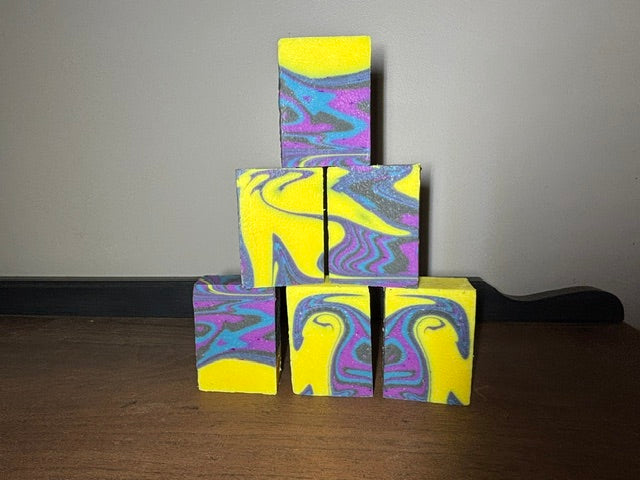 Stack of soap bars colored bright yellow with a blue, purple, and black swirl design.
