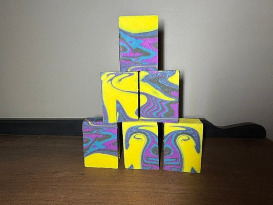 Stack of soap bars colored bright yellow with a blue, purple, and black swirl design.